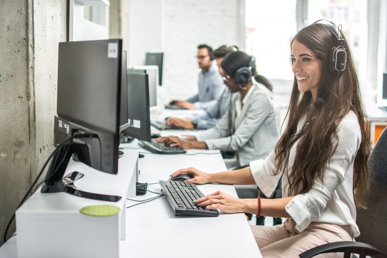 Smiling young businesswoman working with colleagues in a call center office, technical support operators.